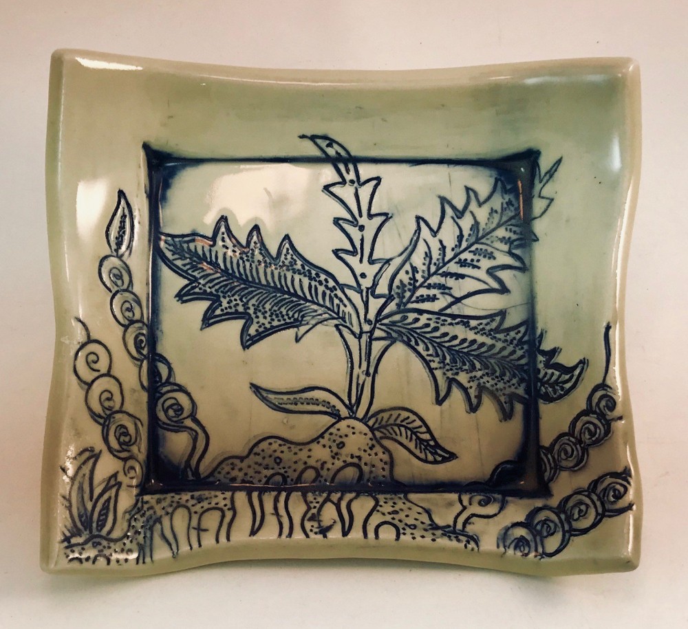 Shallow square celadon dish with a dandelion-like plant drawn in cobalt line, framed by a border of spirals and grasses