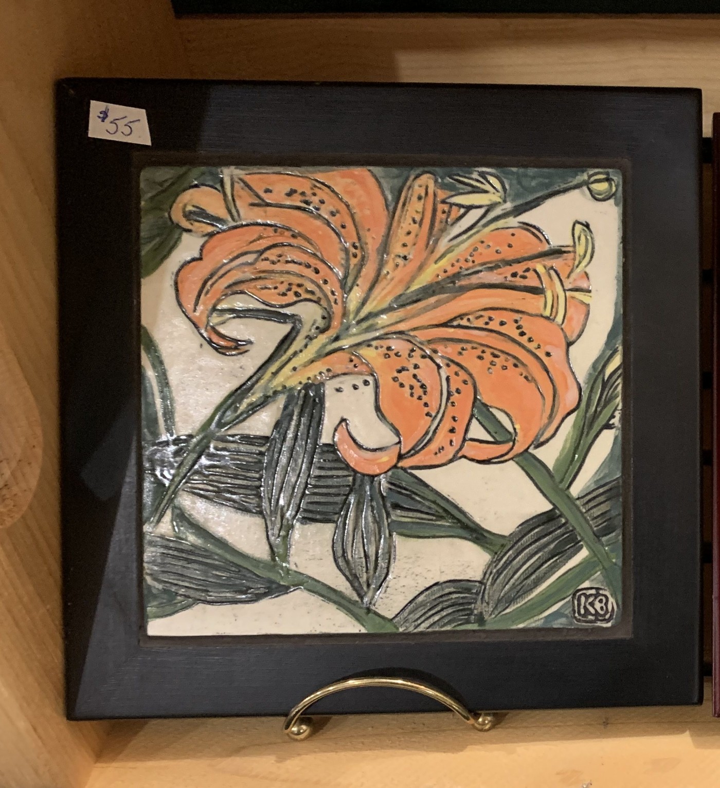 Glazed tile of an orange tiger lily with dark green leaves, in a black wooden frame