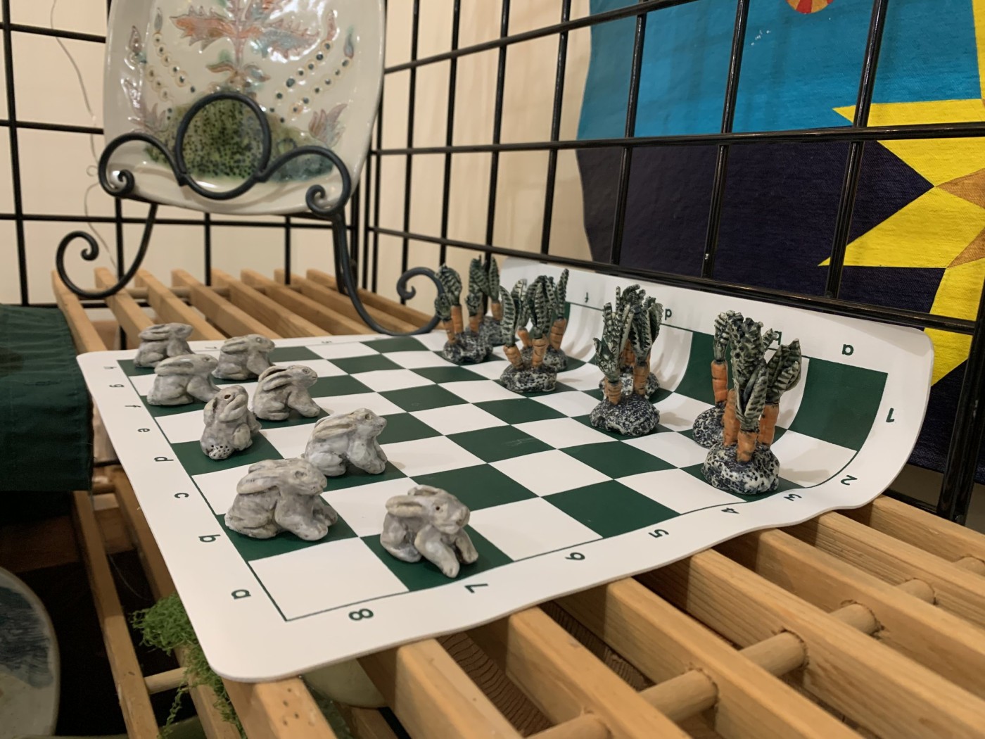A checker set of small clay figures on a board — rabbits face ranks of carrots with green tops