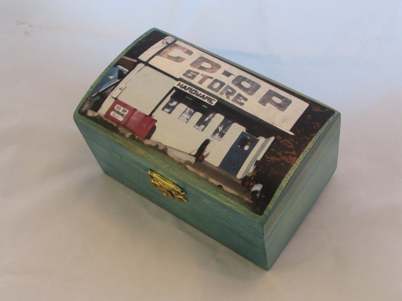 Small hinged box painted teal, the lid showing the Sointula Co-op Store front with its hardware sign